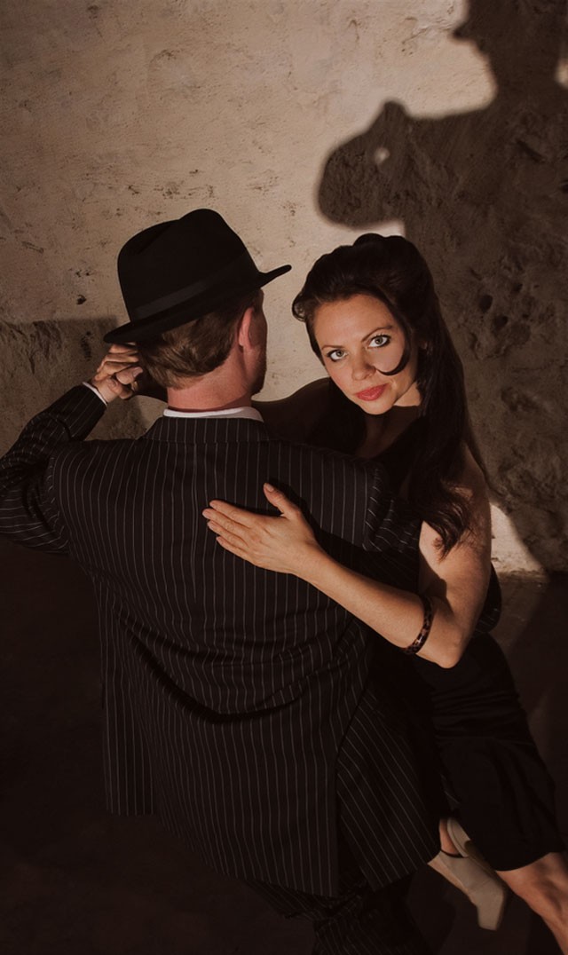 Tango tanzendes Paar im dunklen Kellergewölbe mit einem Akkordion-Spieler an ihrer Seite
